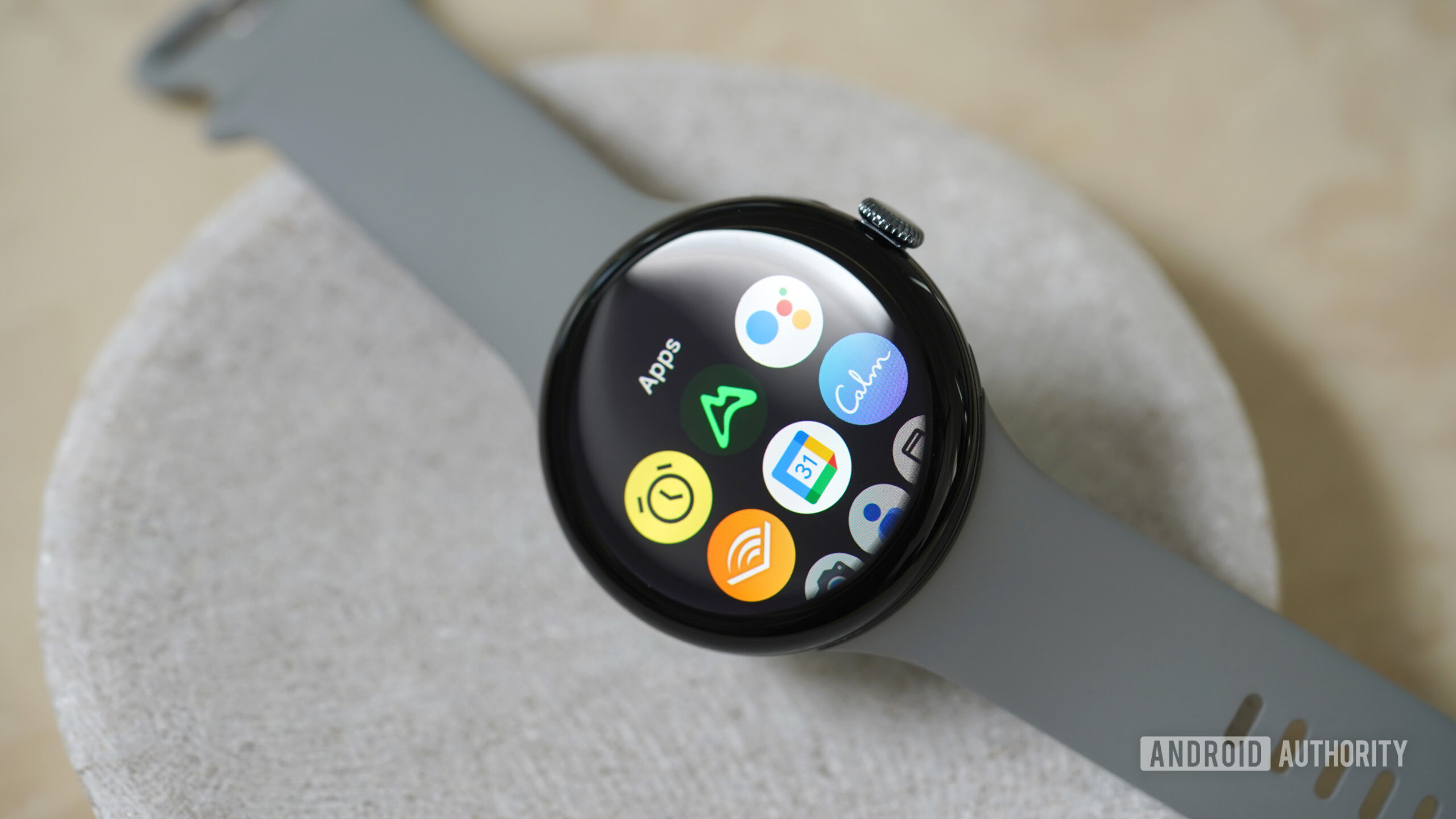 Ένα Google Pixel Watch 3 στηρίζεται σε ένα πέτρινο πιάτο, εμφανίζοντας τη βιβλιοθήκη εφαρμογών του.