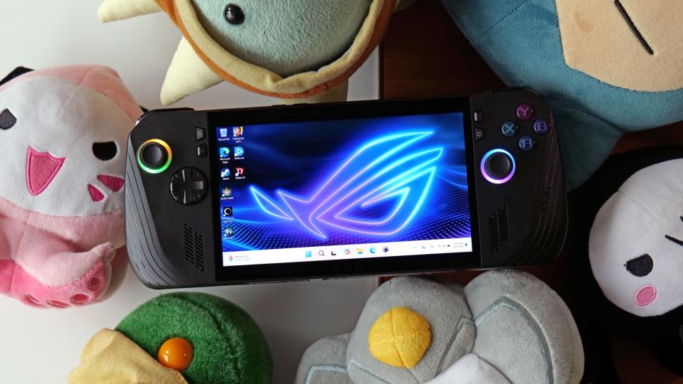 A black ASUS ROG Ally X gaming handheld rests with its screen facing the camera on top of a set of Pokemon plushies.