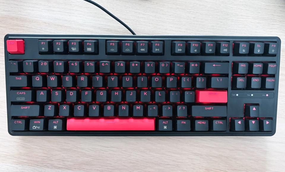 A black keyboard with red backlighting, the Keychron C3 Pro, sits on a light brown desktop.